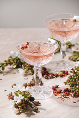 Crystal glasses of pink rose champagne, cider or lemonade with dry rose buds. Blossom cherry branches above. Pink marble background