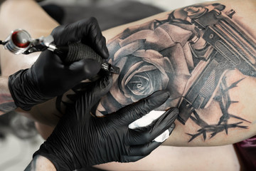 Fototapeta na wymiar Close up image of the bearded tattoo male artist makes a tattoo on a female leg