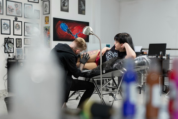 Professional tattoo artist makes a tattoo on a young girl's leg