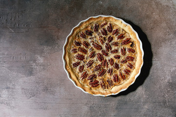 Fresh home baking classic american pecan caramel pie in white ceramic baking dish over grey texture background. Flat lay, space