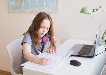 Cute schoolgirl doing homework during her online lesson at home