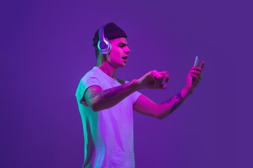 Listen to music with smartphone, dancing. Caucasian man's portrait isolated on purple studio...