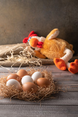 Brown and white chicken eggs in a straw nest on wooden background. Next to a chicken toy sleeping. Vertical orientation