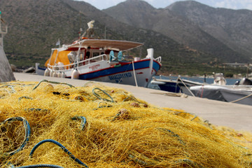 closeup tangled yellow old fishing net necessary equipment of any fisherman for fishing on a concrete pier against the backdrop of mountains, sea, lighthouse and fishing boats