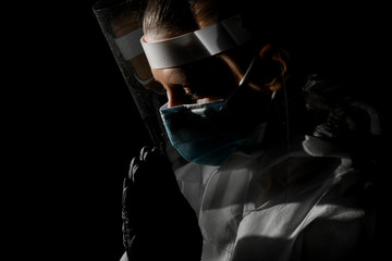 woman in medical protective clothing stands in pose of prayer.