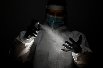 female nurse in medical protective clothes sprays disinfectant on hands