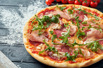 Baked pizza with salami, prosciutto and chicken with red sauce and melted cheese on a black wooden background in a composition with ingredients. Top view