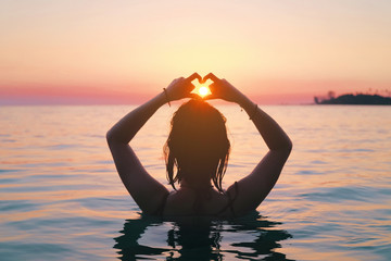Back view of asian woman making heart sign in the sea. Vacation vitality healthy living concept. Silhouette hand in heart shape.