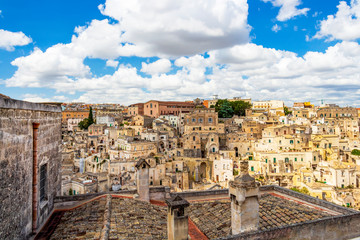 Fototapeta na wymiar Matera old town cityscape behind a chimney with famous chimney cap, beautiful chimney decoration on a rooftop in Matera, Province of Matera, Basilicata Region, Italy under scenic cloudy summer sky