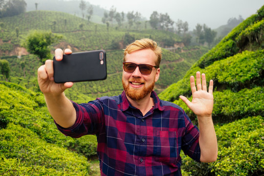 bloger redhaired ginger male enjoying morning taking selfie pictures on camera of smartphone in India chai plantations Munnar