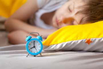 Focus on alarm clock. Child sleeping in bed on pillow with alarm clock in the morning.