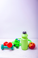 Green bottle of water, sports towel and exercise equipment isolated against a white background and wooden table.