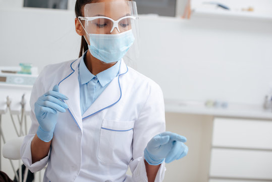 African American Dentist In Medical Mask, Face Shield And Latex Gloves Pointing With Finger In Clinic