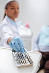 selective focus of african american dentist in latex glove taking dental instrument