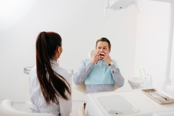 back view of african american dentist sitting near scared patient touching face