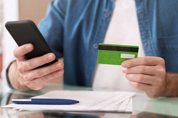 Internet banking, e-commerce and online trading concept. Closeup of young caucasian man holding mobile phone and credit card while paying bills at home