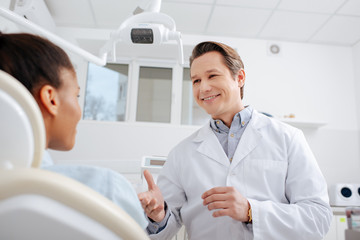 selective focus of happy dentist looking at african american patient and gesturing in clinic