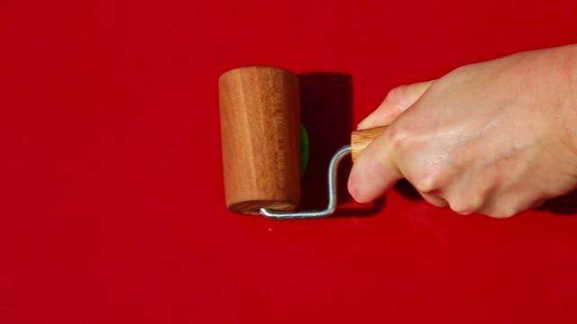 top view on woman hands slowly roll out with wooden roll small round piece of bright green homemade marzipan mass on red table surface