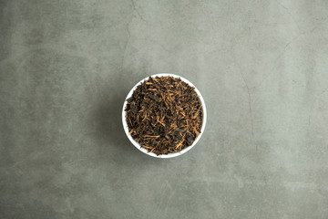 Dry black tea leaf in white porcelain bowl on concrete, stone background. Traditional, healthy and organic beverage. Top view, flat lay.