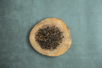 Dry black tea leaf in wooden platter on concrete background. Traditional, healthy and organic beverage. Top view, flat lay.