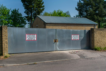 A large pair of closed metal gates.  The red warning sign reads "Please do not park in front of these gates. Entrance in constant use".