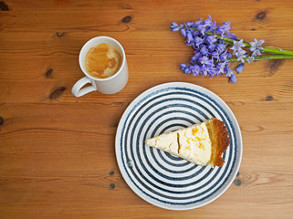 Flat lay consisting of slice of pie on the plate, cup of coffee and blue flowers on the wooden table. 