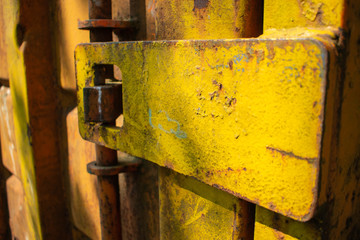 A heavy duty opening mechanism to enter a construction container.  The industrial unit is old and rusted and painted a bright yellow colour.