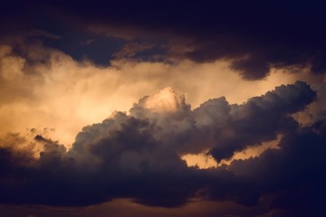 Dark, dramatic nimbus clouds at sunset, lit by the last rays of sunlight before a storm.