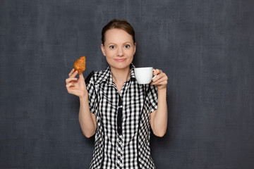 Portrait of happy girl holding coffee cup and croissant in hands