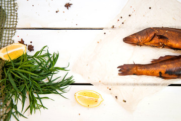 Golden smoked fish with spice, green and lemons on white wood plank background