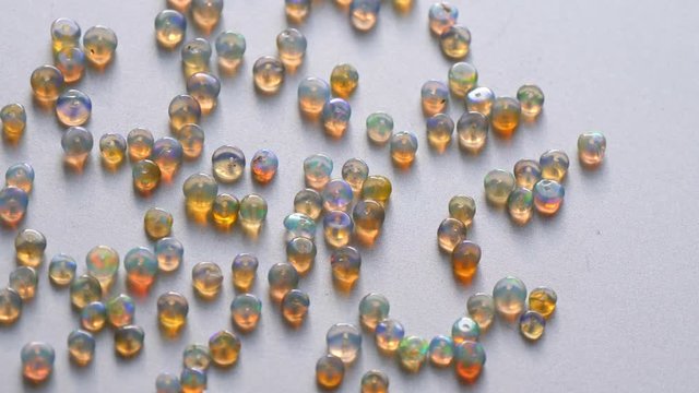 Opals gemstone from Ethiopia rotates on light background. White fire opals with rainbow like fire. Natural fire Ethiopian opal, small stones to create jewelry. Handmade stone jewelry. A pile stones.
