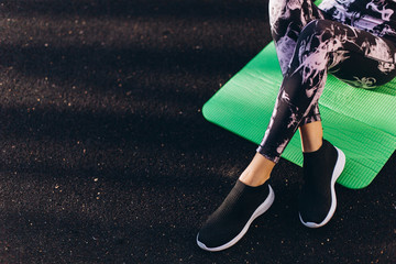 Legs of sporty fitness girl sitting on sport ground in gym