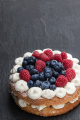 Victoria sponge cake with whipped cream and berries on top on black stone background