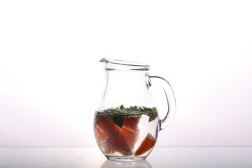 glass carafe with water grapefruit and mint on a white background