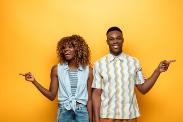happy african american couple pointing with fingers on yellow colorful background