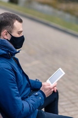 Protective mask on a person's face. A man reads a book in the street.