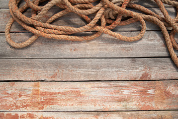Obraz premium A rusty rope lies on top of a wooden background. Jute has a fibrous surface, there is a non-textured empty space for text.