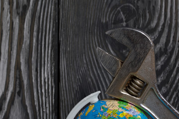 The adjustable spanner head lies on the globe. Against the background of brushed pine boards. Symbol of World Labor Day.