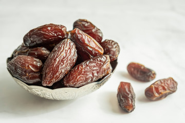 Raw date fruit ready to eat in silver bowl on a white marble background. Traditional, delicious and healthy ramadan food.