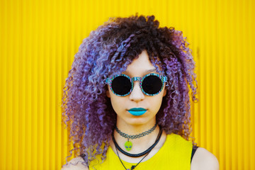 Portrait of cool woman with sunglasses outdoors at summer season. Millennial woman with urban casual style isolated on yellow background. Hair dyed with psychedelic bright colors concept.