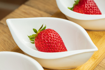 Fresh strawberry fruit in white dish on wooden background.