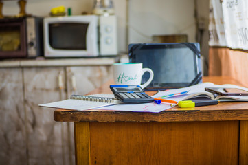 On the home table are stock and finance charts with a calculator, a coffee mug, a pencil, a marker pen, two notebooks, a smartphone and a tablet for remote work. Work at home.