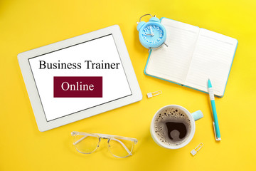 Modern tablet with text BUSINESS TRAINER ONLINE on yellow background, flat lay