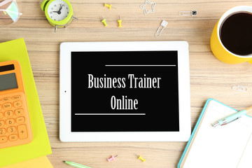 Modern tablet with text BUSINESS TRAINER ONLINE on wooden background, flat lay