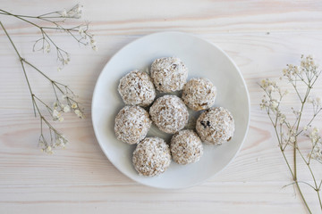 Homemade sweets, protein bars or energy balls on a white plate with white flowers, healthy breakfast, top view