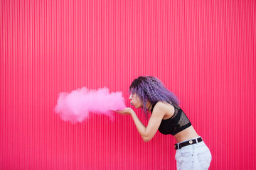 Artistic and creative ethnic young woman blowing with air a big pink smoke cloud. Art and...