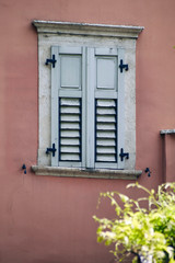 Fototapeta na wymiar Italian window on the dark pink wall facade with closed wooden grey color classic shutters