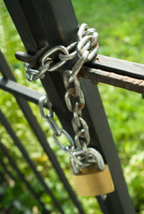 A metal gate closed and secured with a chain and a padlock.