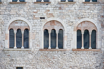 Fototapeta na wymiar Three Italian antique windows on the old castle stone wall facade
