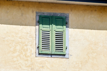 Fototapeta na wymiar Italian window on the yellow wall facade with closed green color wooden classic shutters